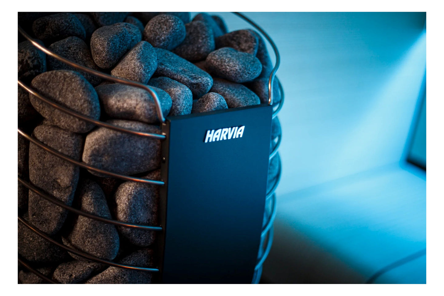Harvia Spirit electric sauna heater filled with dark gray stones, metal grate visible, navy container on blue background