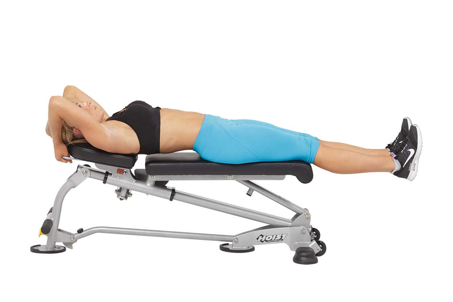 Woman using silver and black Hoist weight bench with blue shorts and black sports top, demonstrating ab exercise position on 