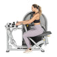 Woman using silver leg press machine with dual handles, wearing black sports bra and lavender leggings on white background