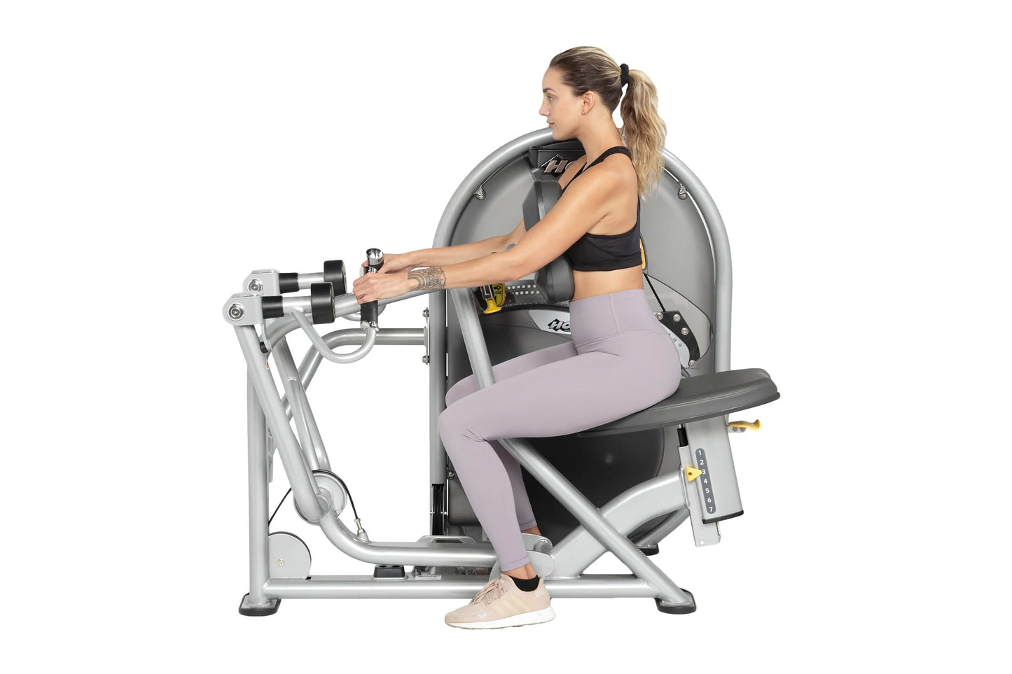 Woman using silver leg press machine with dual handles, wearing black sports bra and lavender leggings on white background