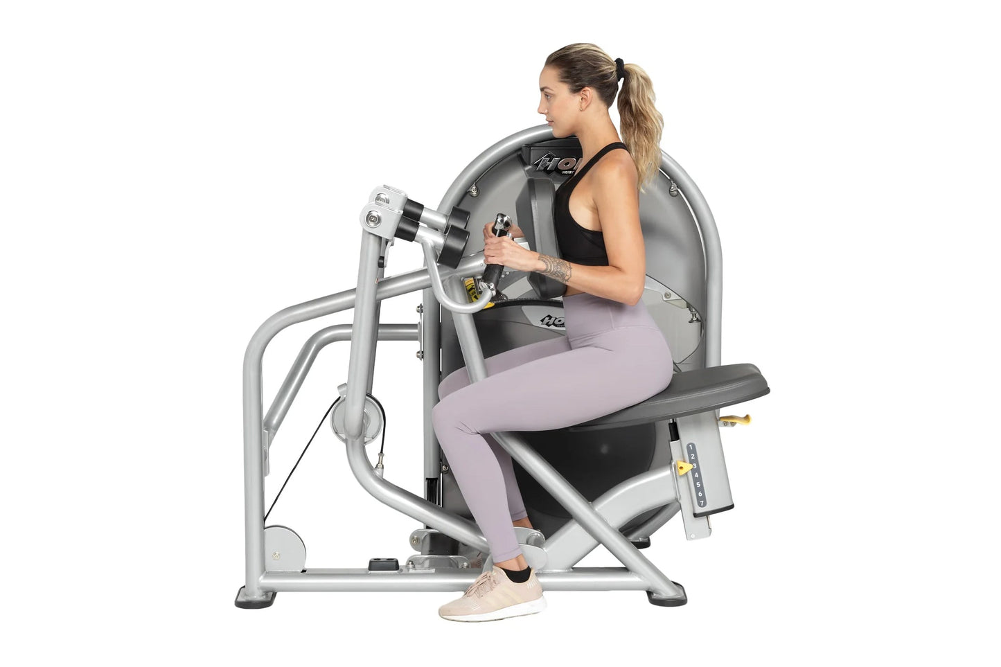 Woman using silver Hoist leg press machine with gray seat, wearing black tank top and lavender leggings, on white background