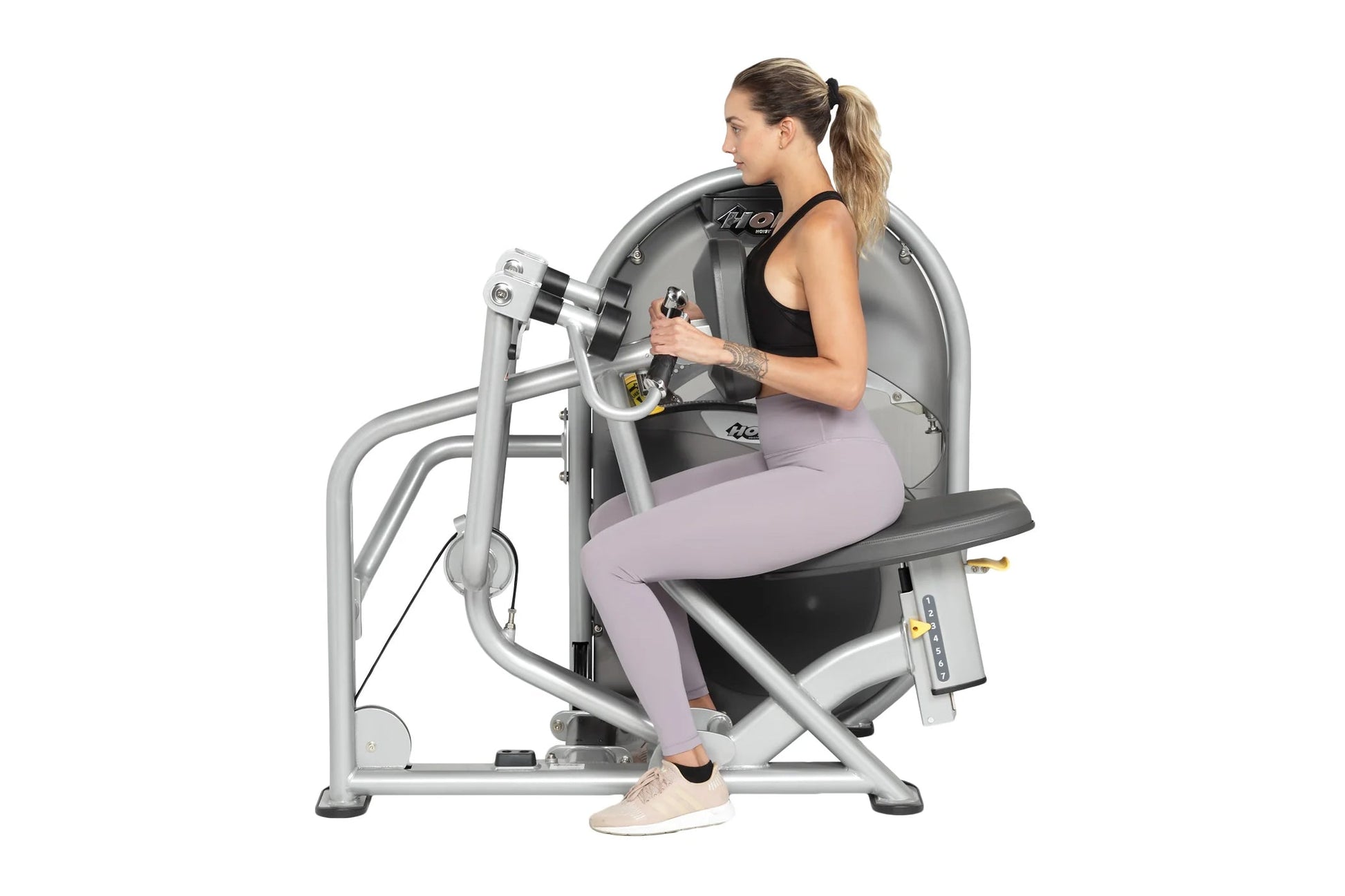 Woman using silver Hoist leg press machine with gray seat, wearing black tank top and lavender leggings, on white background