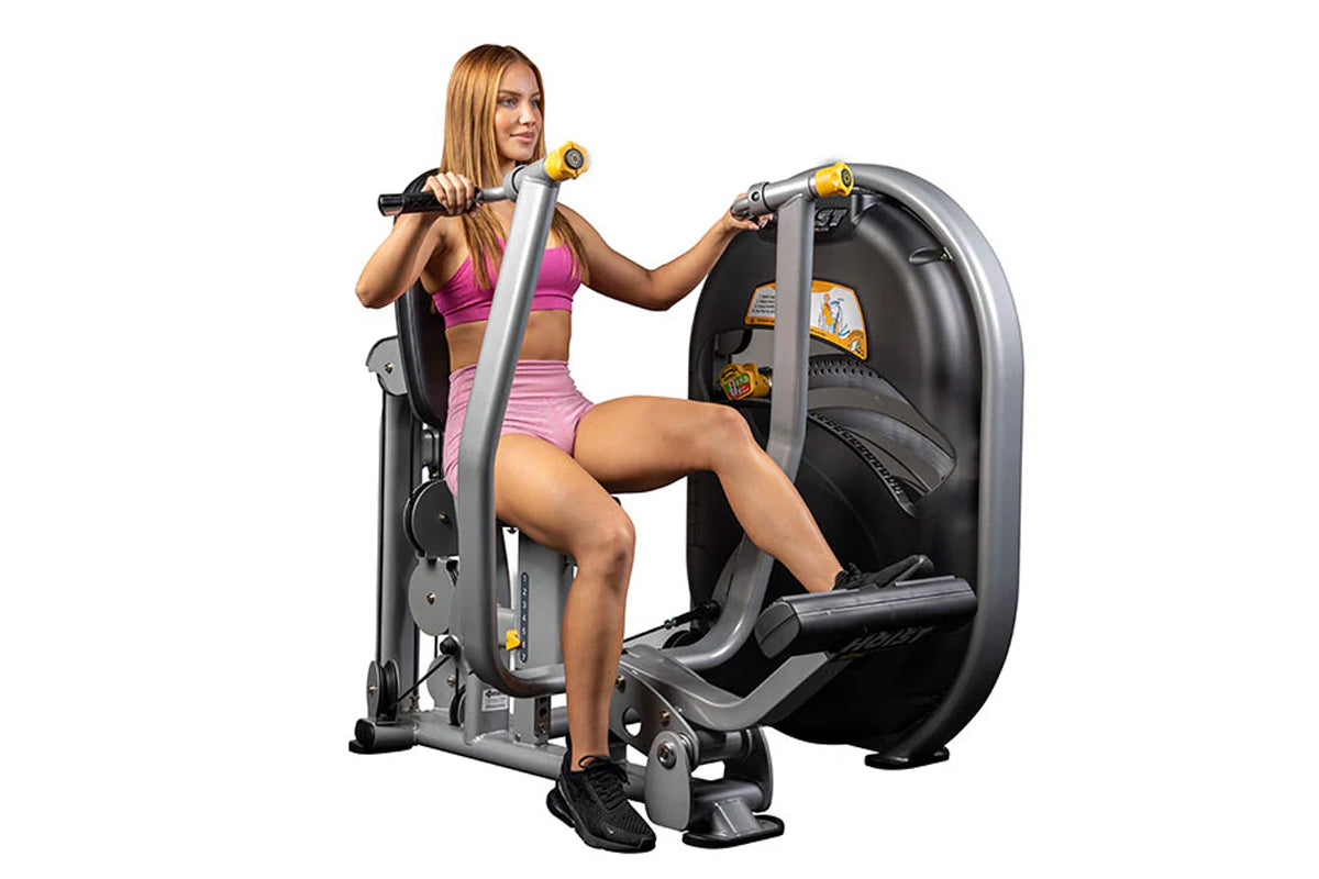 Woman in pink sports bra and shorts using black and silver Hoist chest press machine with yellow handles on white background