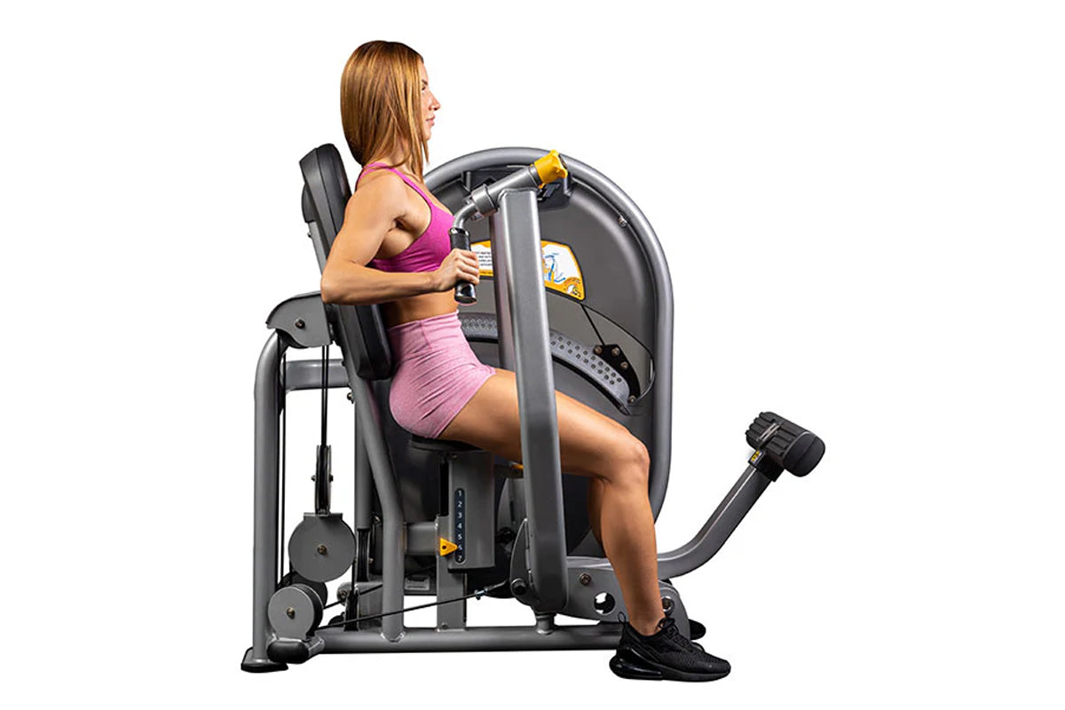 Woman using black and gray Hoist Chest Press machine with yellow accents, wearing pink sports bra and shorts on white backgro