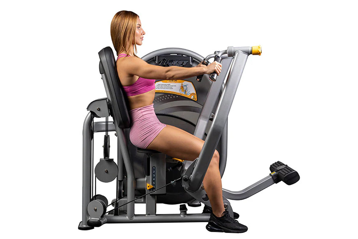 Woman in pink sports bra and shorts using gray and black Hoist chest press machine with yellow handles on white background