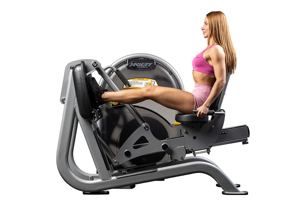 Woman in pink sports bra and shorts using Hoist leg press machine with black and gray frame on white background