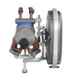 Person using gray and silver leg curl machine with large weighted plate, wearing blue headband and gray shirt, viewed from ab