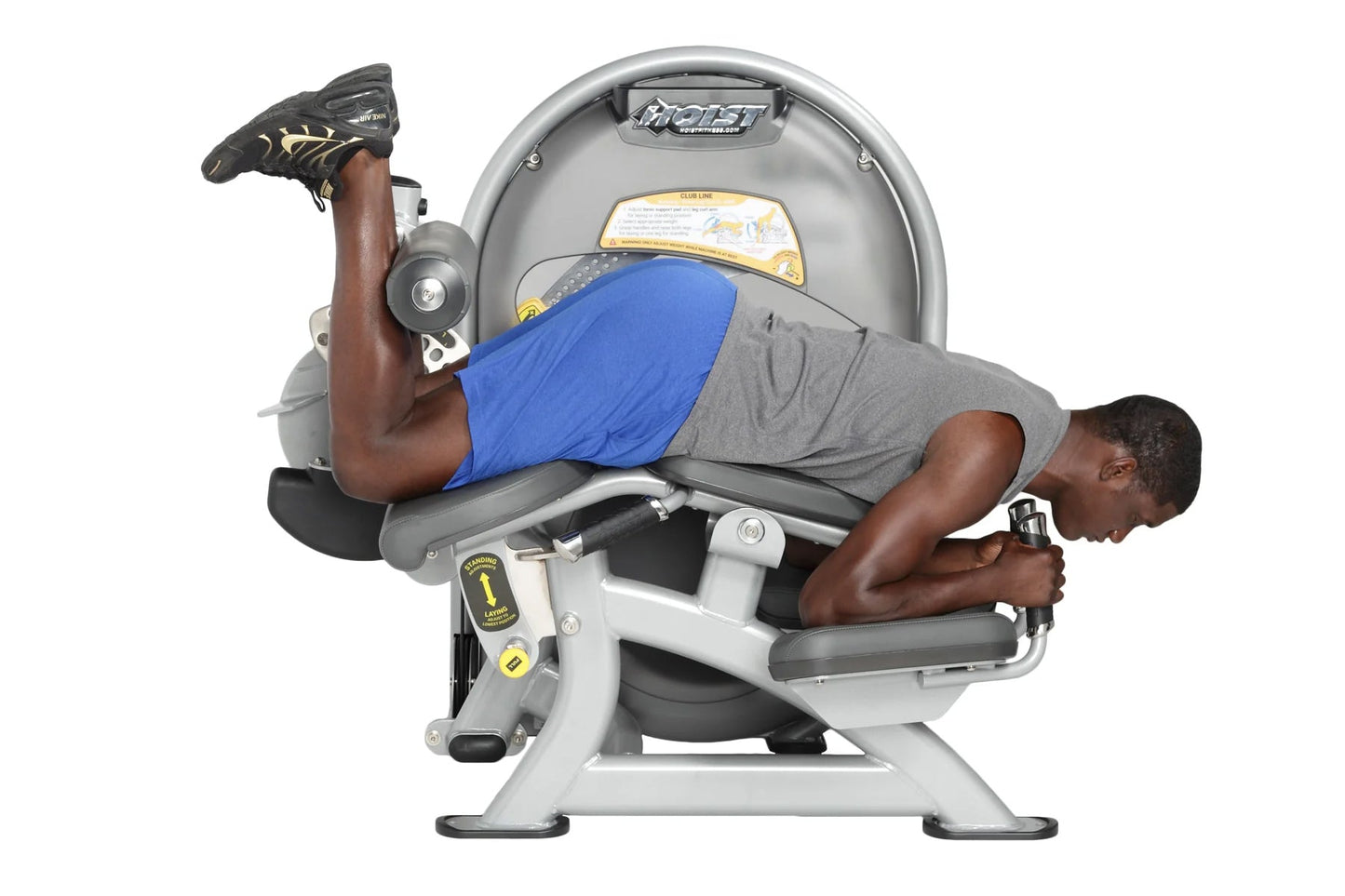 Man using Hoist standing prone leg curl machine with gray frame, blue padded seat, and yellow accents