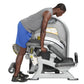 Man using gray and white Hoist Standing Prone Leg Curl machine with blue shorts and gray tank top, demonstrating leg exercise