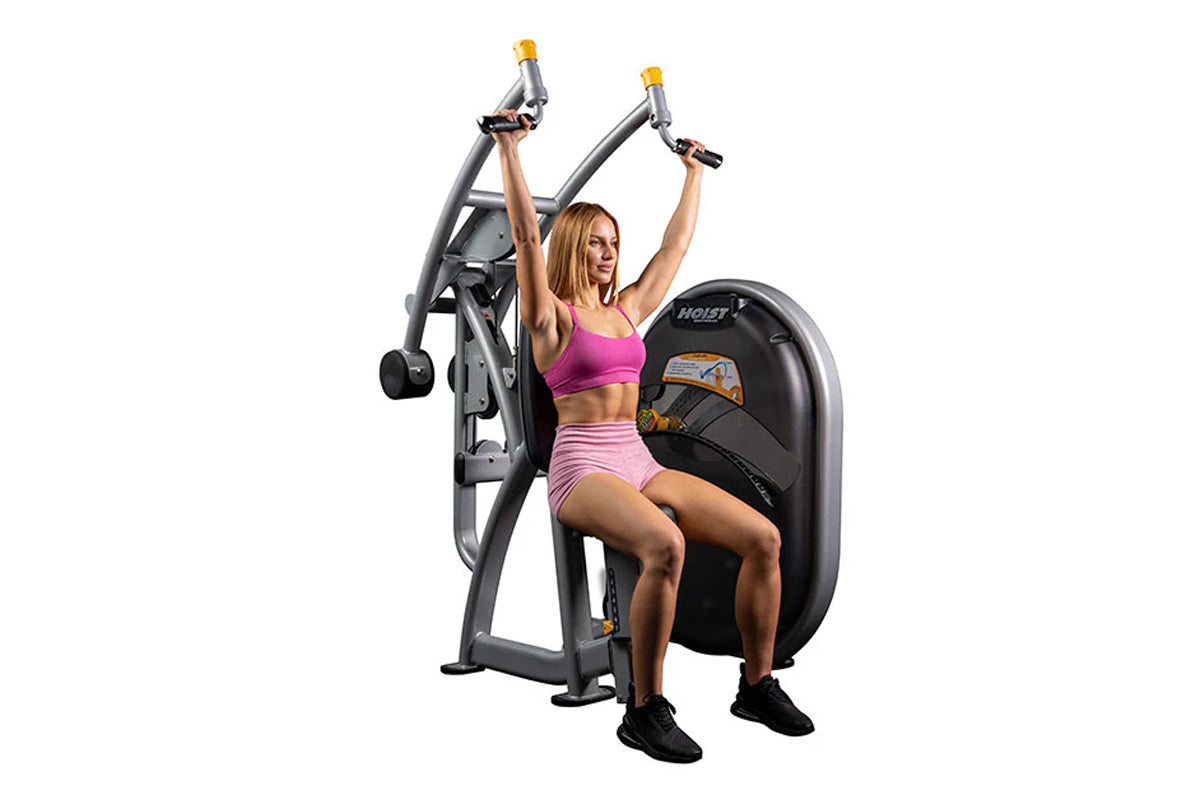 Hoist Club Line Shoulder Press machine with gray frame and yellow handles, demonstrated by model in pink sports bra and short