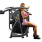 Woman in pink sports bra and shorts using black and gray Hoist Club Line shoulder press machine on white background