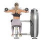 Woman performing lateral raise with dumbbells on Hoist machine, wearing black sports bra and lavender leggings, on white back
