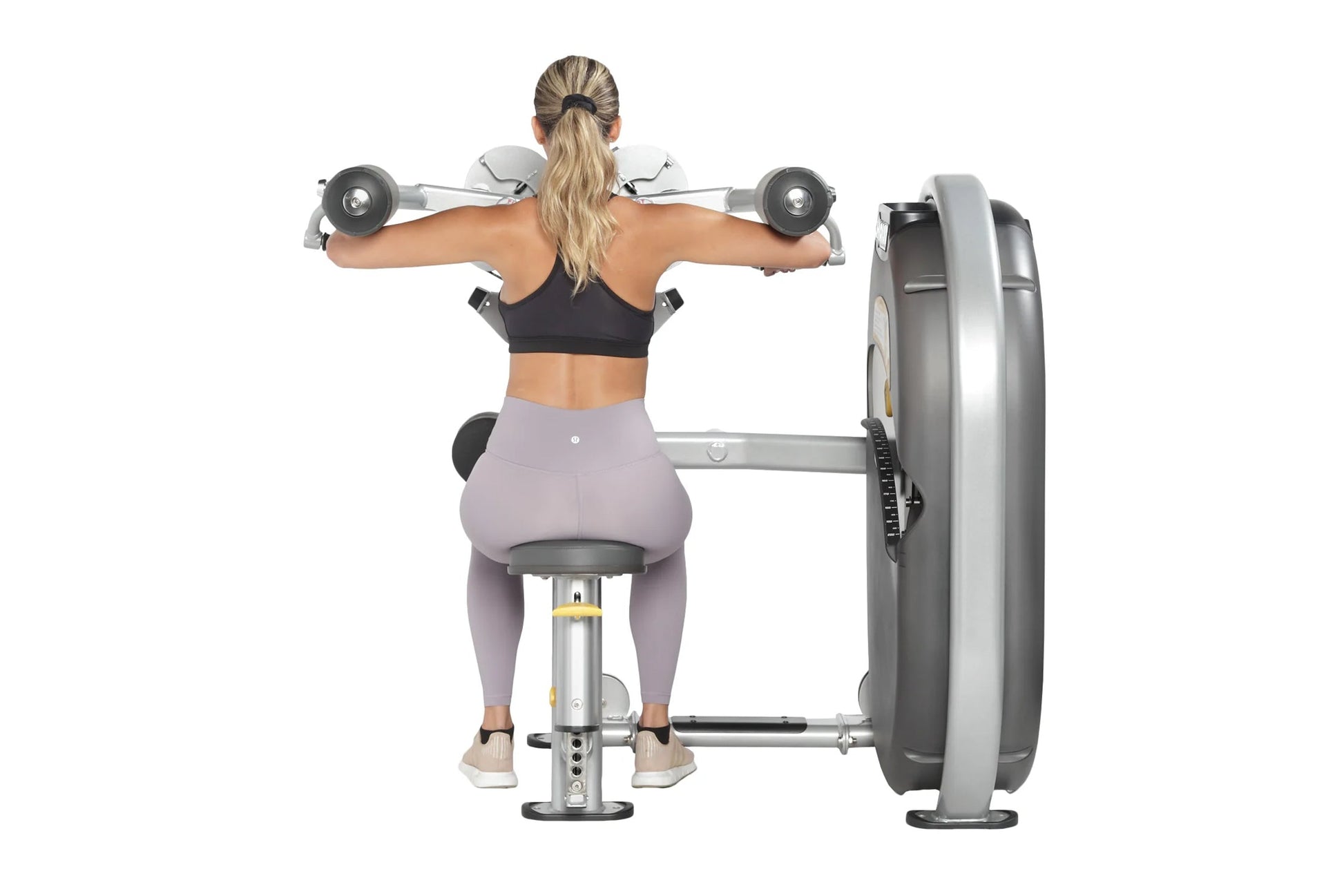 Woman performing lateral raise with dumbbells on Hoist machine, wearing black sports bra and lavender leggings, on white back