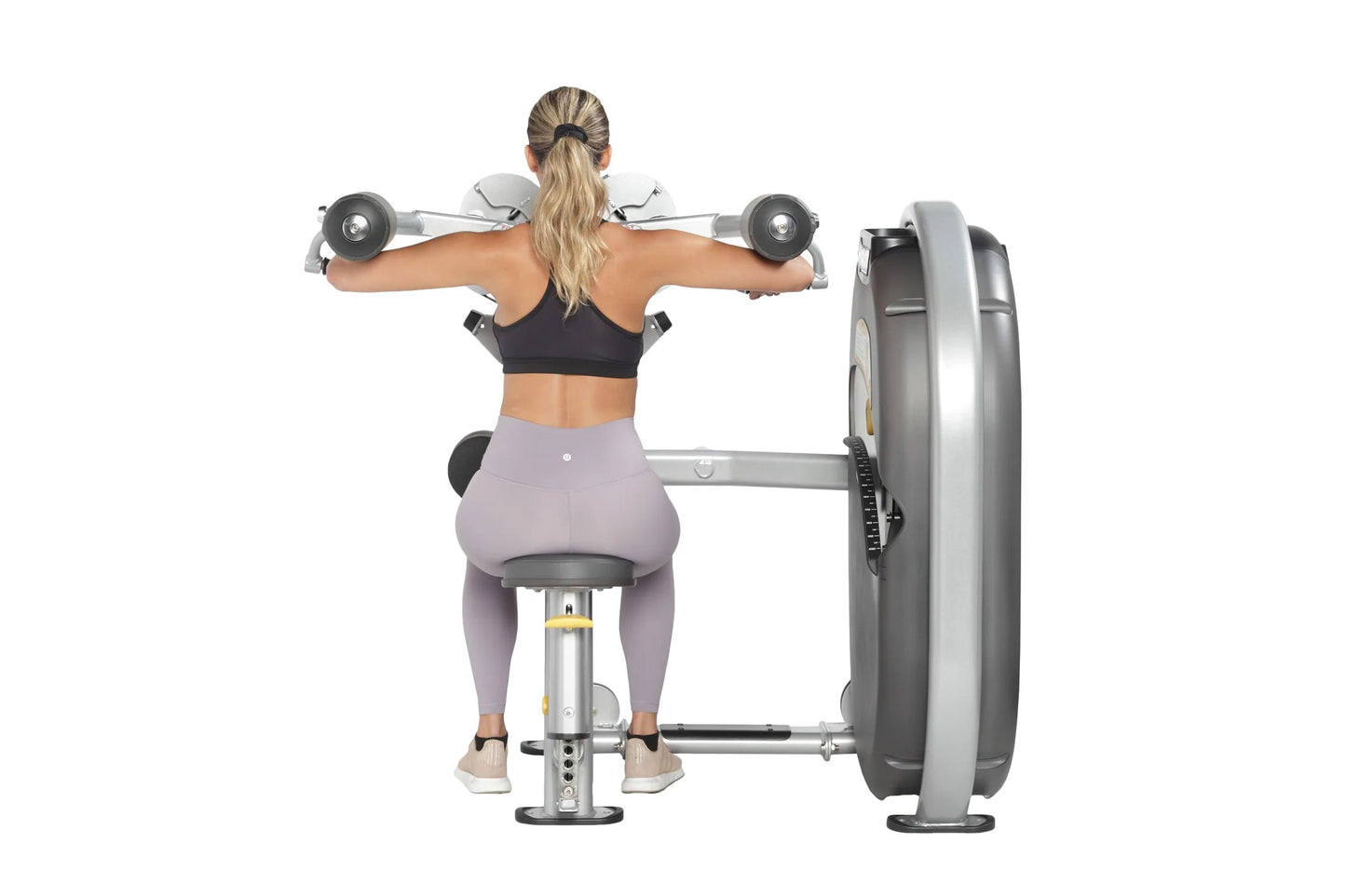 Woman performing lateral shoulder raise with dumbbells on Hoist weight machine, wearing black sports bra and lavender legging