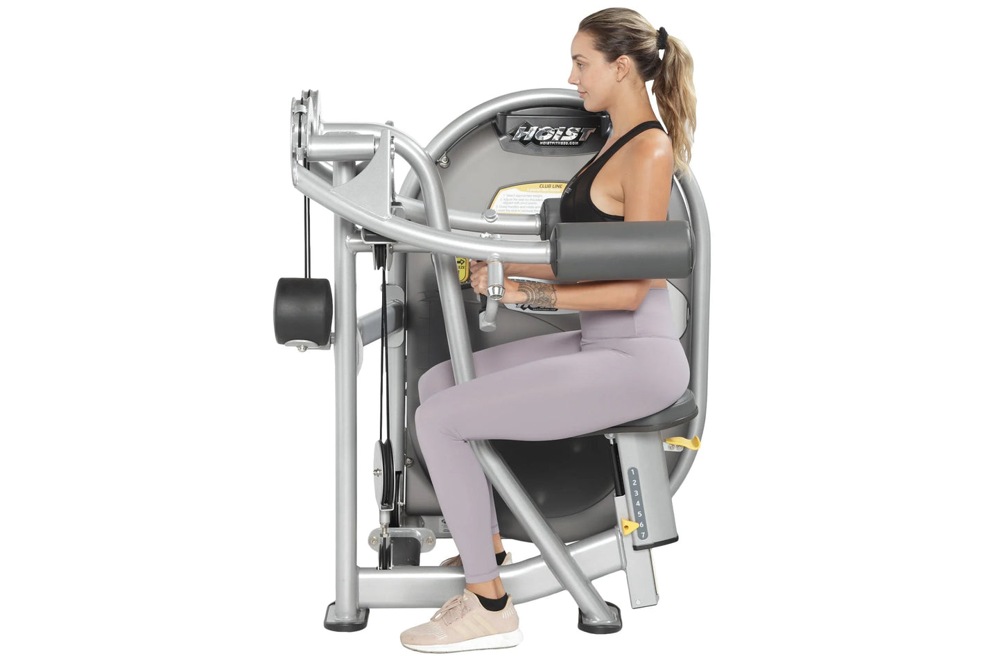 Woman using Hoist Lateral Raise machine with silver metal frame and black padded seat and armrests