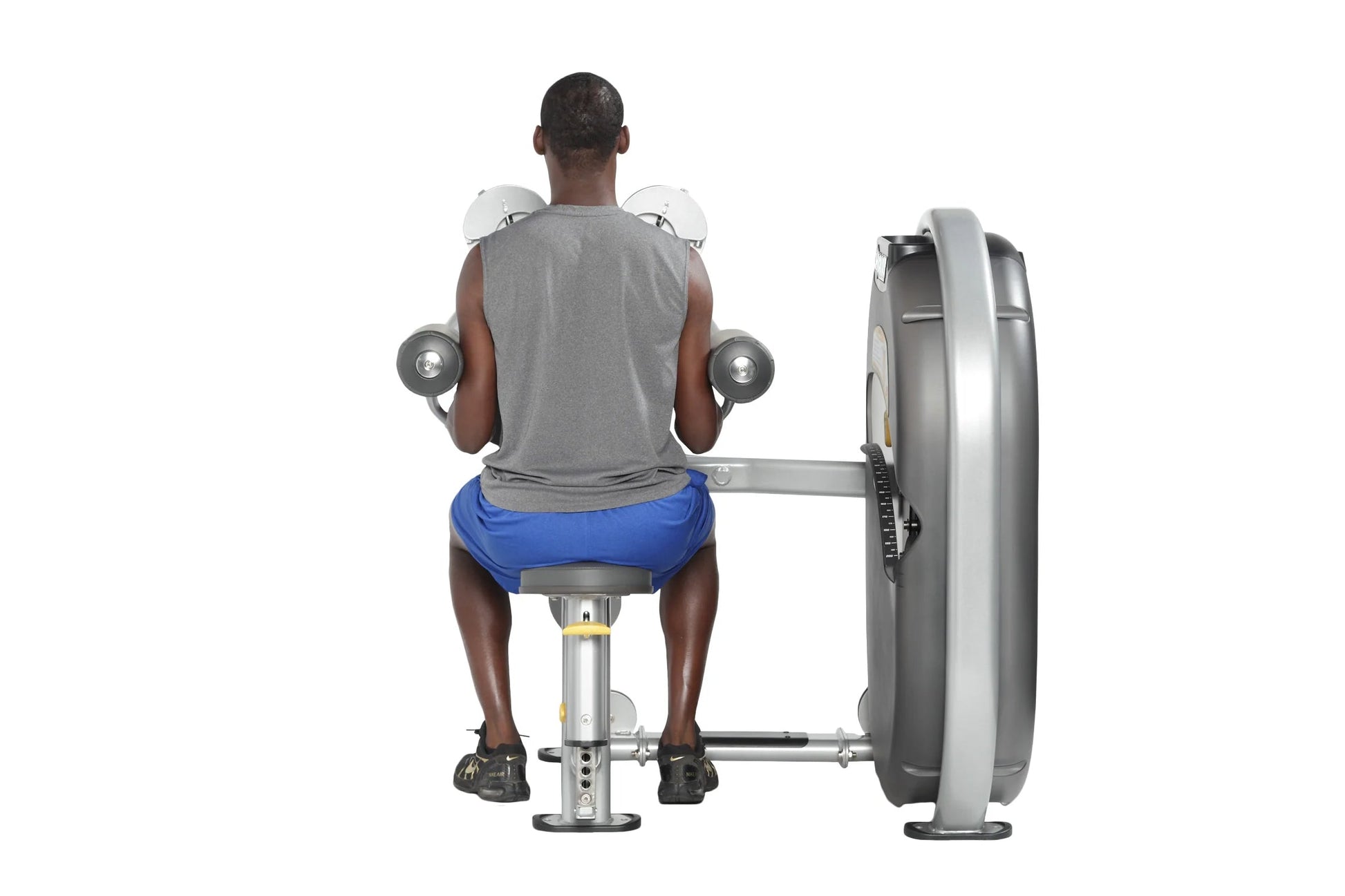 Man seated on blue bench performing dumbbell lateral raise exercise with gray weight machine on white background