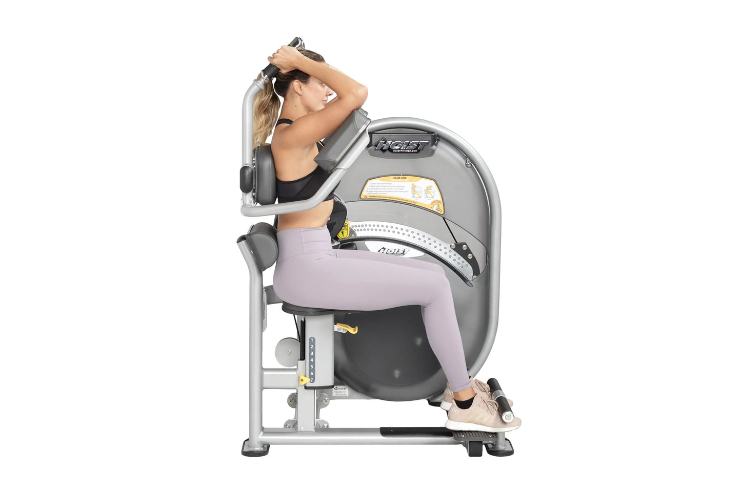 Woman using gray and black abdominal exercise machine with padded seat, arm handles, and foot platform on white background