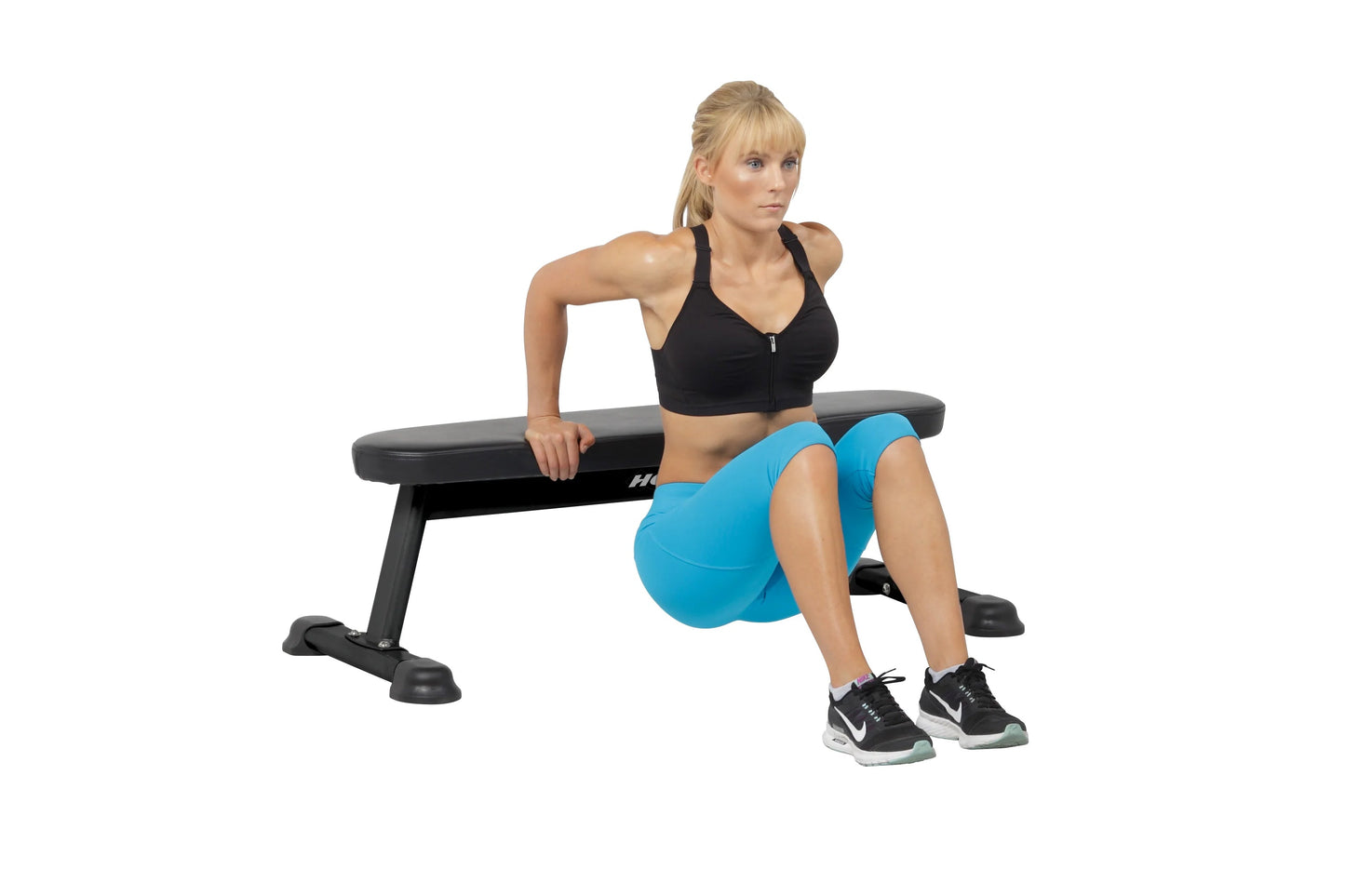 Model wearing black halter sports bra and blue shorts on Hoist flat utility bench with black and gray padding, demonstrating 