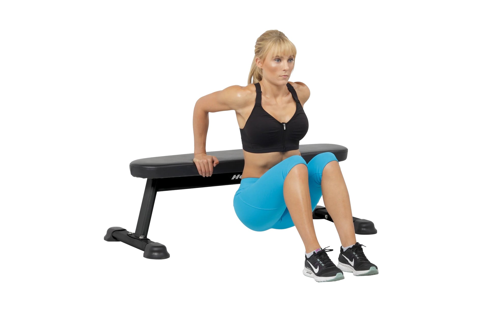 Model wearing black halter sports bra and blue shorts on Hoist flat utility bench with black and gray padding, demonstrating 