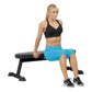 Black padded flat utility bench with sturdy frame, worn by model in black sports bra and blue shorts during exercise demonstr