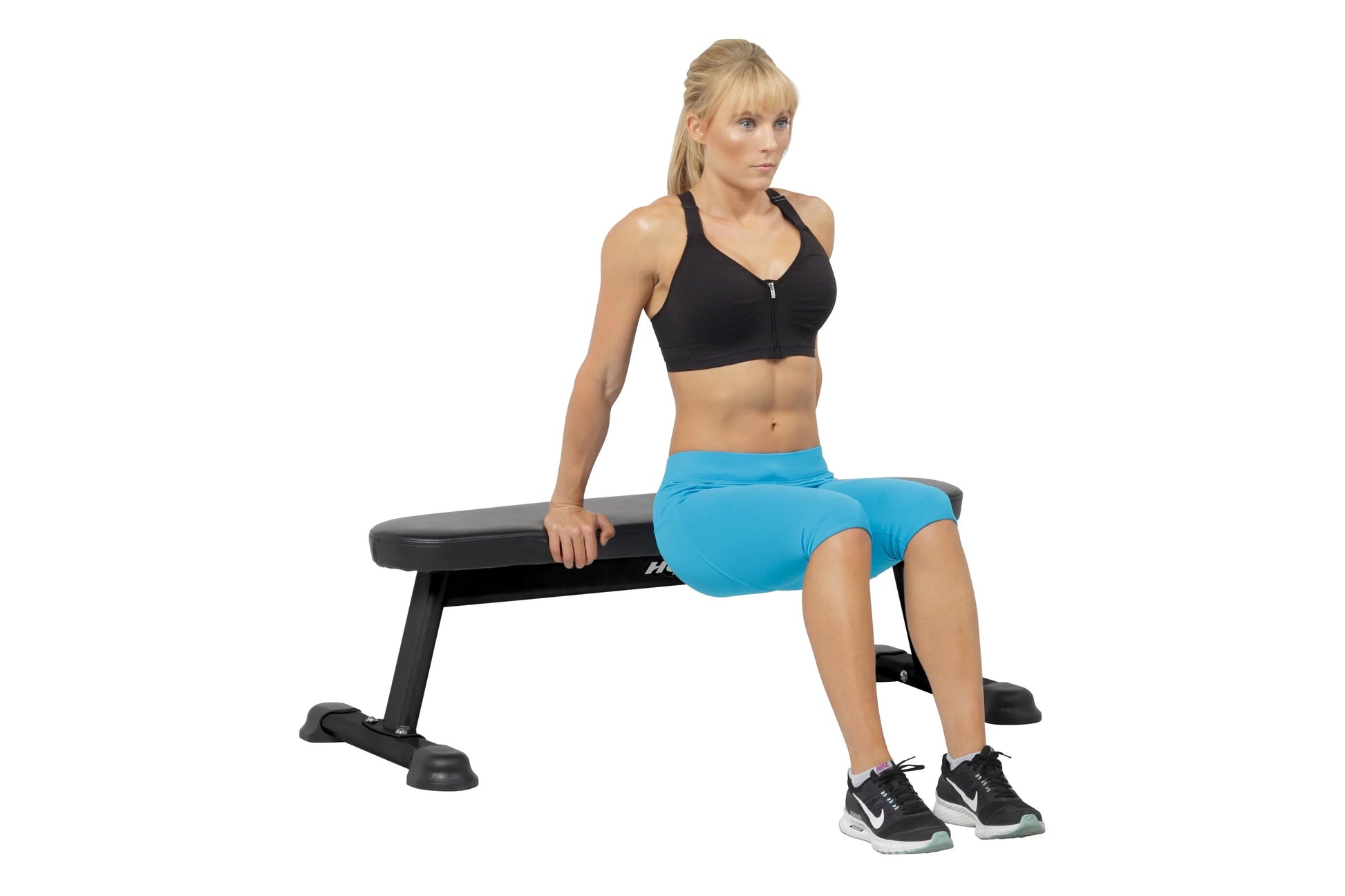 Black padded flat utility bench with sturdy frame, worn by model in black sports bra and blue shorts during exercise demonstr