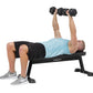 Man performing dumbbell chest press on black Hoist flat utility bench, wearing light blue shirt and black shorts