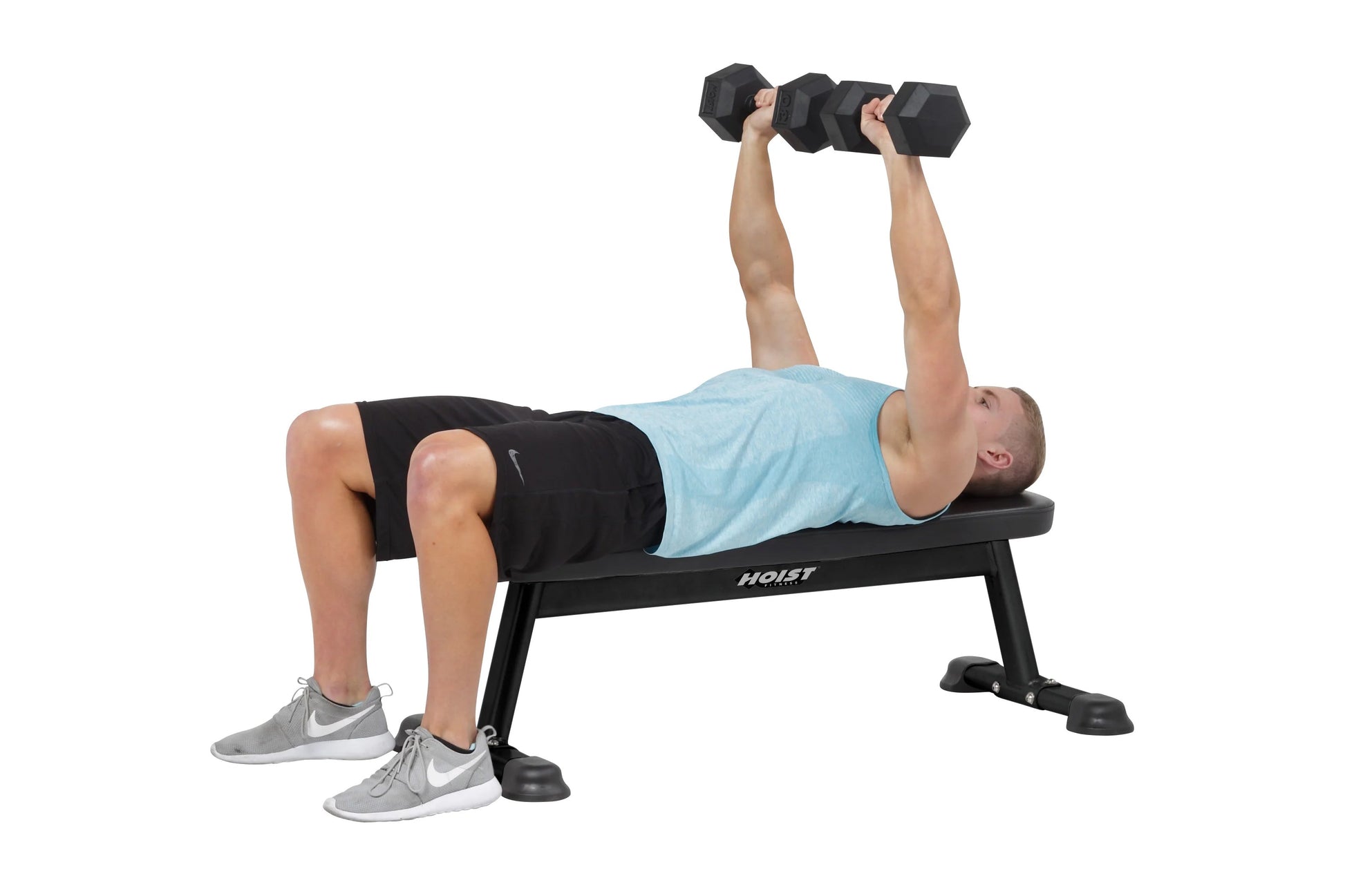 Man performing dumbbell chest press on black Hoist flat utility bench, wearing light blue shirt and black shorts