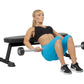 Woman exercising on black Hoist utility bench, wearing blue shorts and black sports top, holding dumbbell barbell on white ba