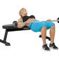 Woman performing barbell bench press on black Hoist flat utility bench with 30-pound dumbbells, wearing blue shorts and black