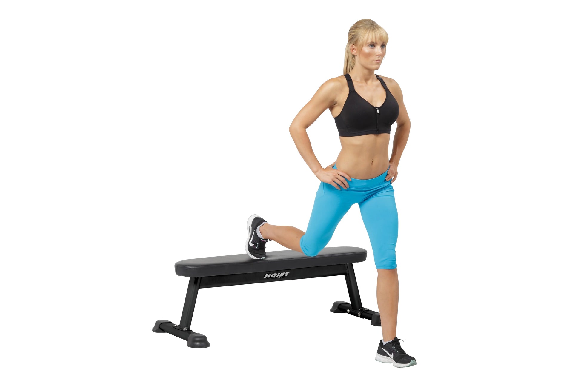 Woman in black sports bra and turquoise capri leggings performing a lunge exercise on a black Hoist flat utility bench agains