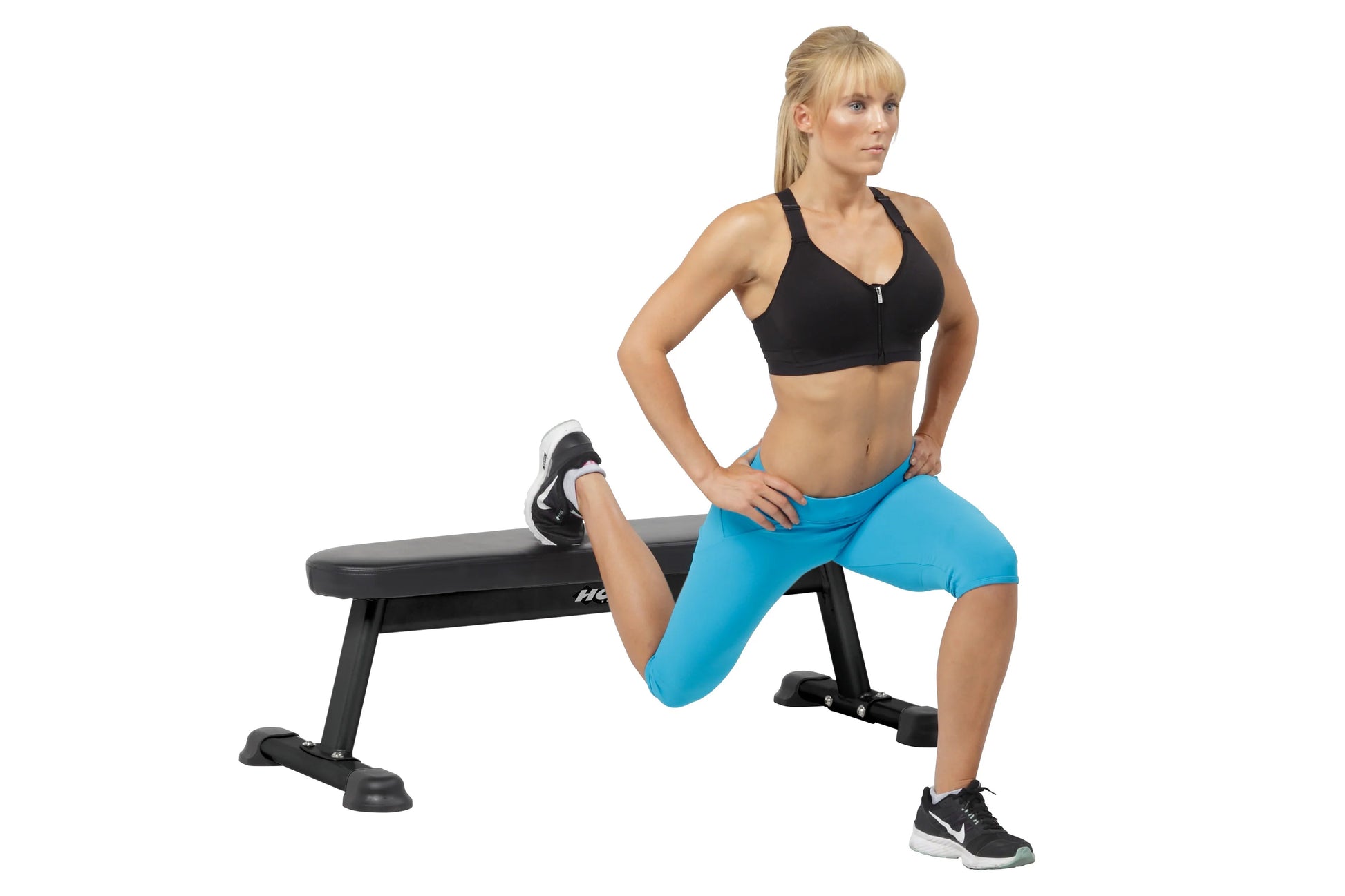 Model wearing black sports bra and bright blue shorts, demonstrating lunge exercise on Hoist flat utility bench with black fr