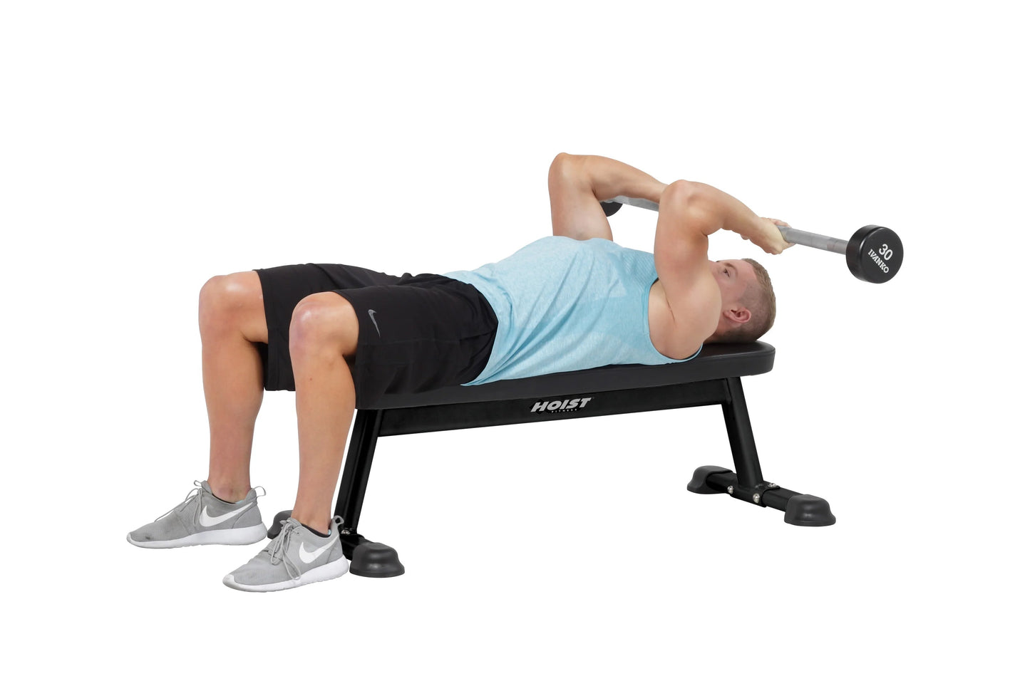 Man performing dumbbell chest press on black Hoist utility bench, wearing light blue tank top and black shorts