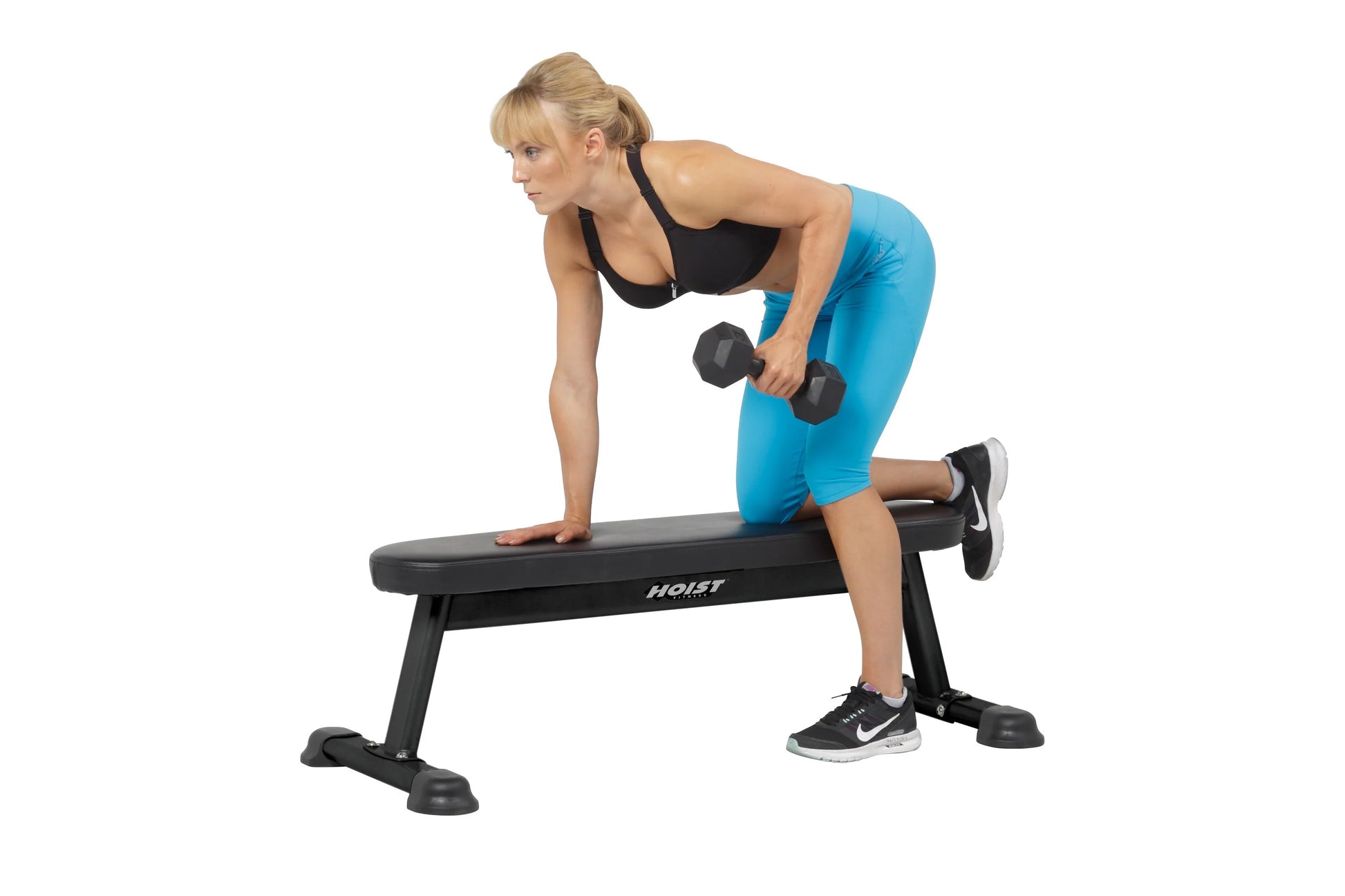 Woman performing dumbbell exercise on black Hoist flat utility bench, wearing blue leggings and black sports bra