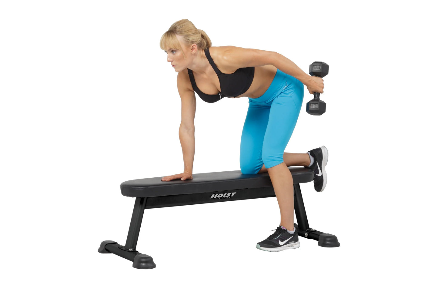 Woman performing dumbbell exercise on black Hoist flat utility bench, wearing blue capri leggings and black sports bra