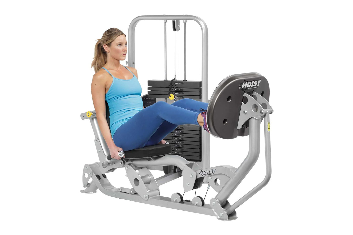 Woman in blue tank top and navy leggings using silver and black Hoist leg press machine with weight stack on white background
