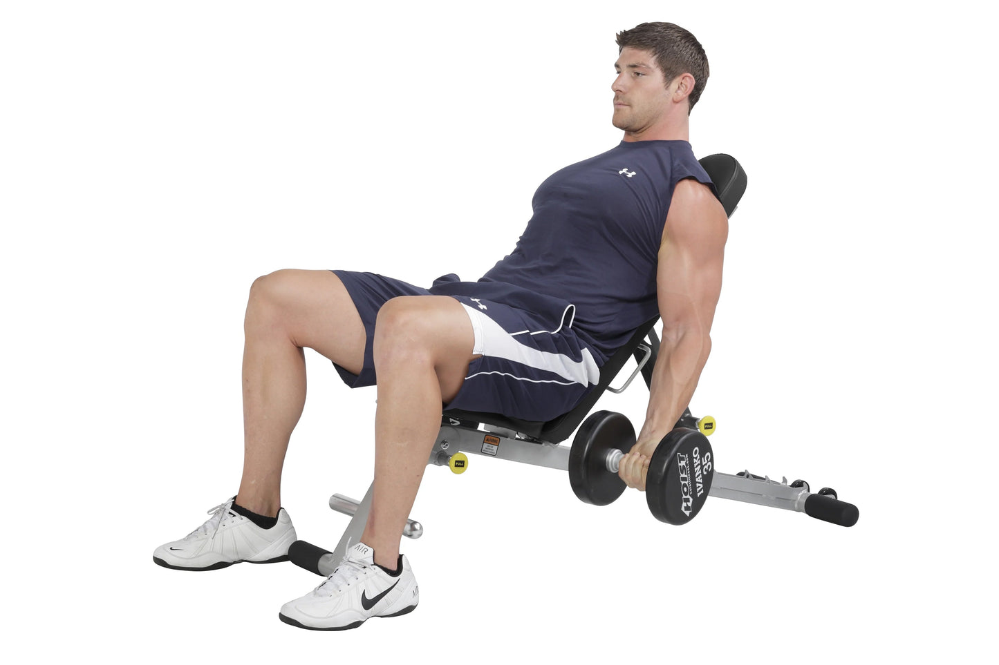 Man seated on navy and white folding weight bench performing dumbbell exercise with black weights, white sneakers on white ba