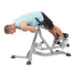 Man using gray Hoist ab and back Roman hyperextension bench with light blue shirt, performing abdominal exercise on white bac