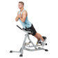 Man wearing light blue tank top and black shorts using gray and black Hoist Roman hyper bench for core exercise on white back