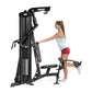 Black multi-station home gym machine with overhead pull-down and leg press, demonstrated by woman in light blue tank top and 