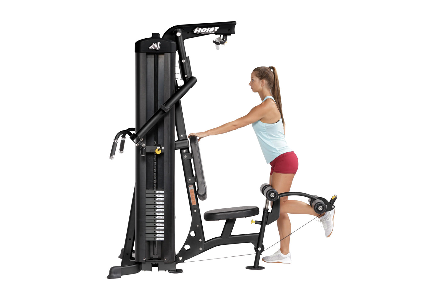 Black multi-station home gym machine with overhead pull-down and leg press, demonstrated by woman in light blue tank top and 