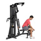 Black Hoist Mi1 home gym machine with weight stack, shown with male model in red shirt performing leg exercise on seated posi