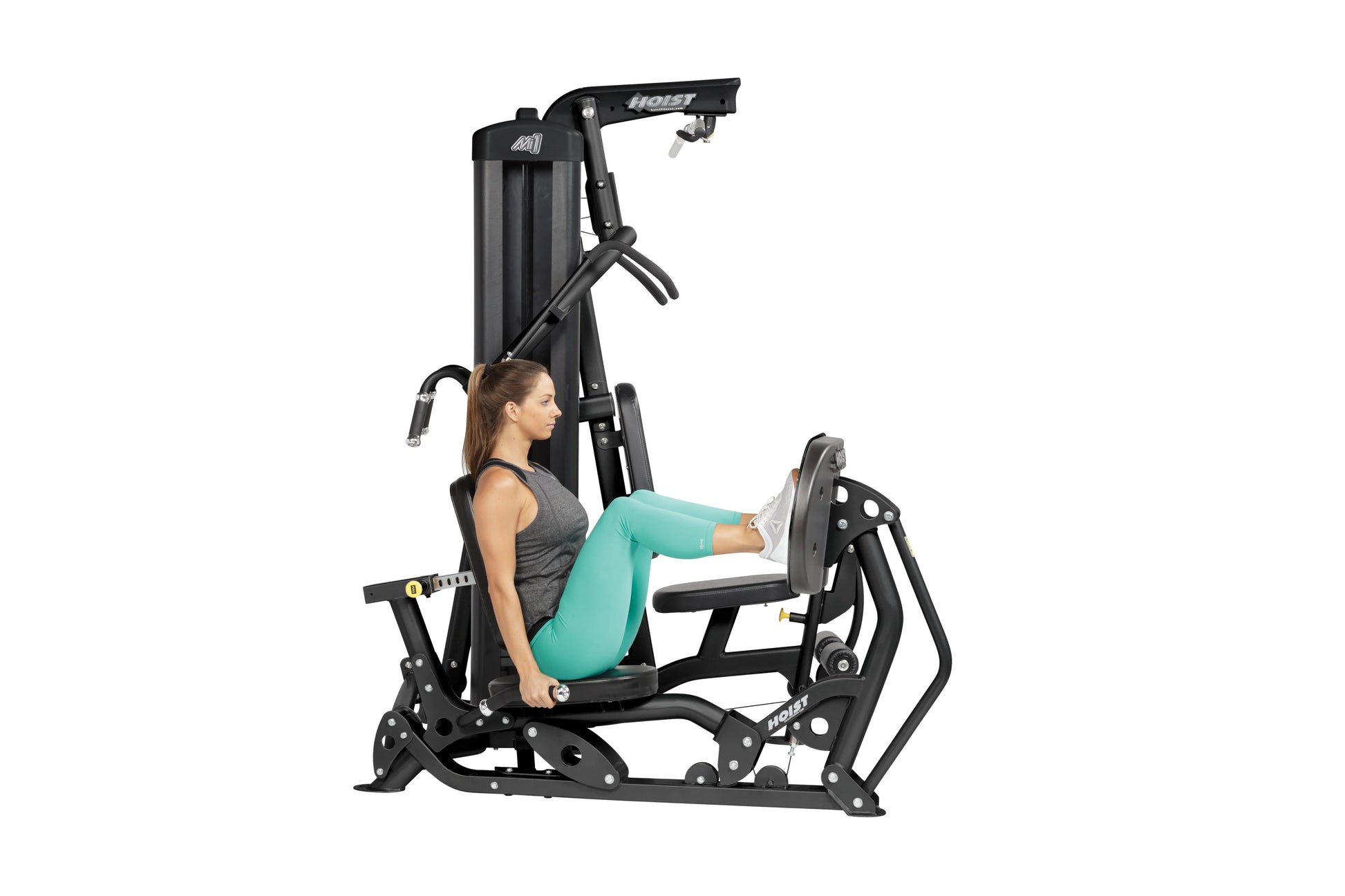 Woman using black Hoist Mi1 home gym machine with leg press, wearing gray tank top and turquoise leggings on white background