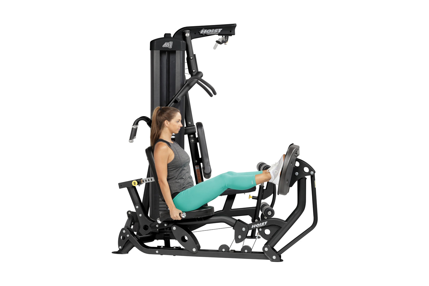 Woman using black Hoist Mi1 home gym machine with leg press attachment, wearing gray tank top and teal leggings, on white bac