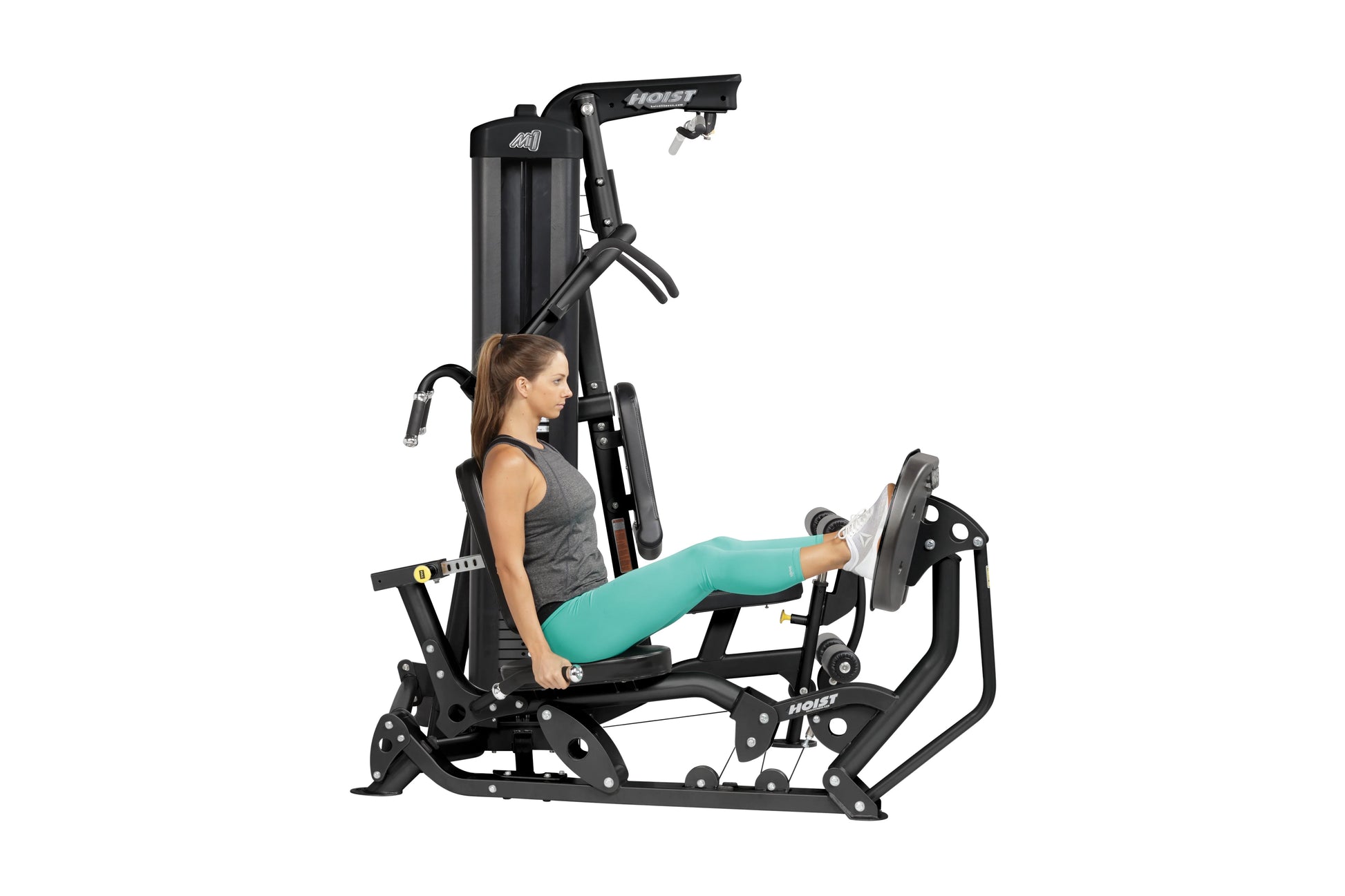 Woman using black Hoist Mi1 home gym machine with leg press attachment, wearing gray tank top and teal leggings, on white bac