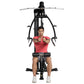 Man in red shirt using black Hoist Mi1 home gym with dual handles and foot pedals, front view on white background