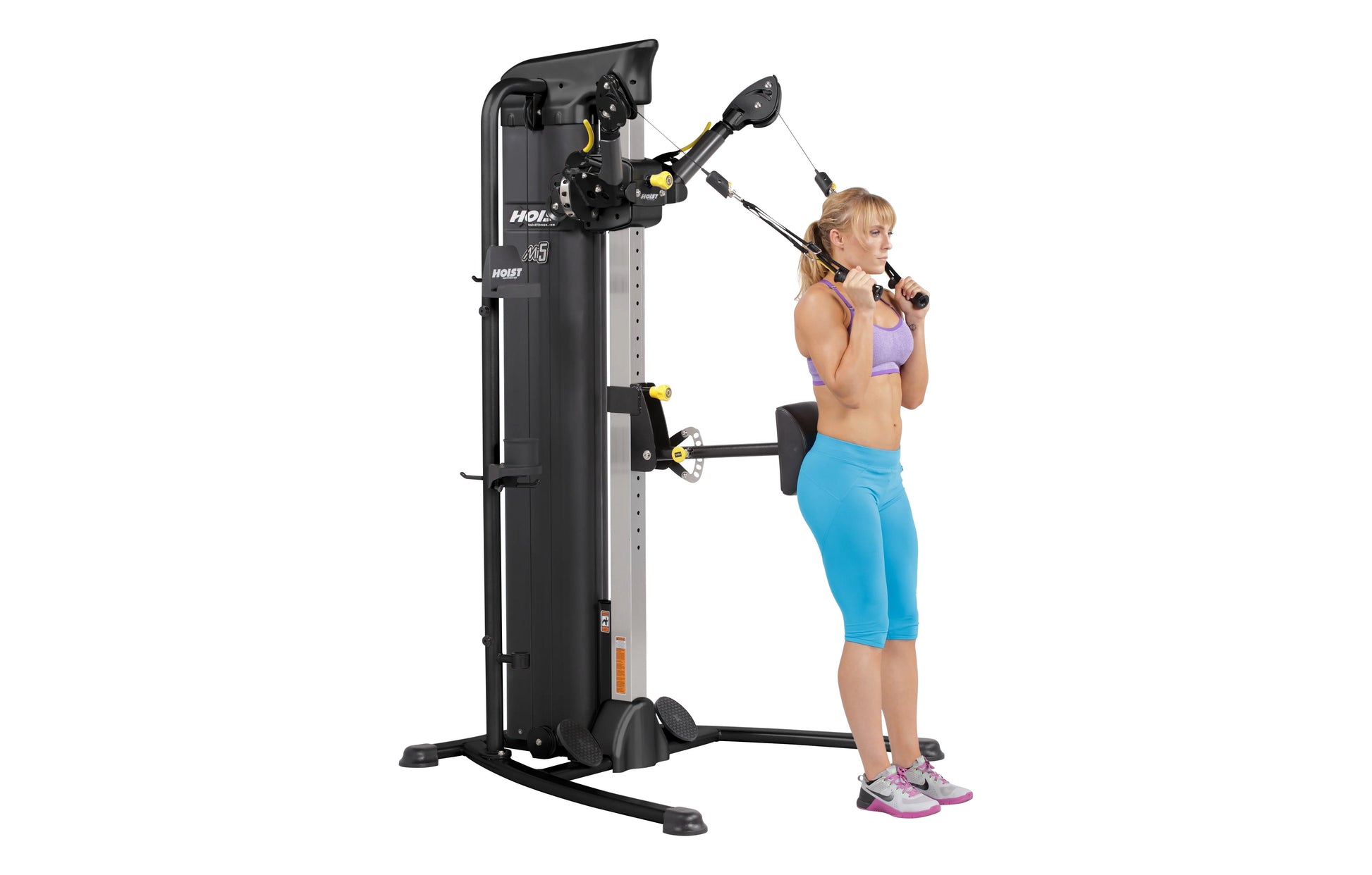Black and yellow Hoist Mi5 functional trainer with dual cable stations, demonstrated by woman in purple sports bra and blue c