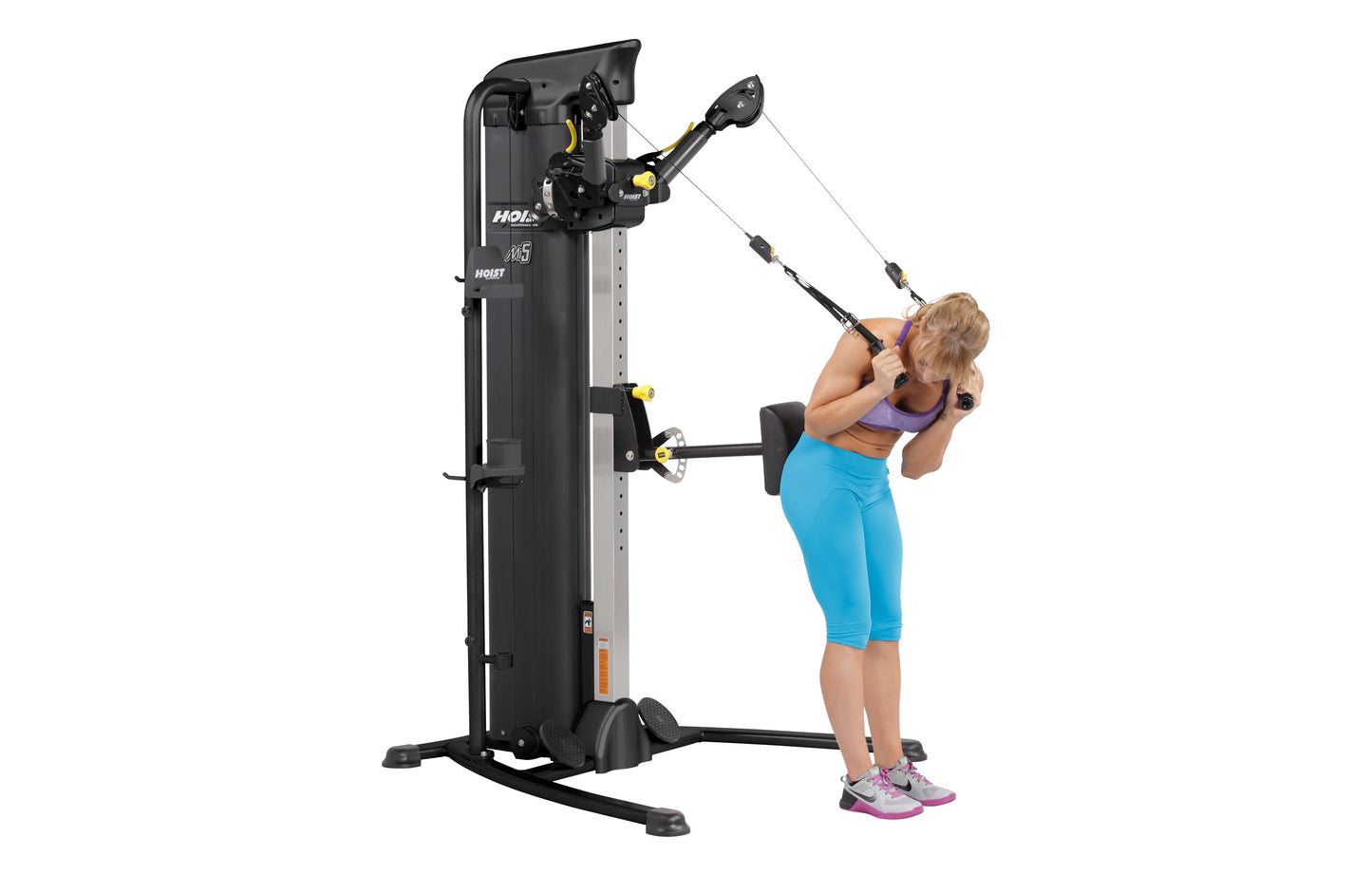 Black and yellow Hoist Mi5 Functional Trainer with dual cable stations, shown with woman in blue capris and purple top perfor
