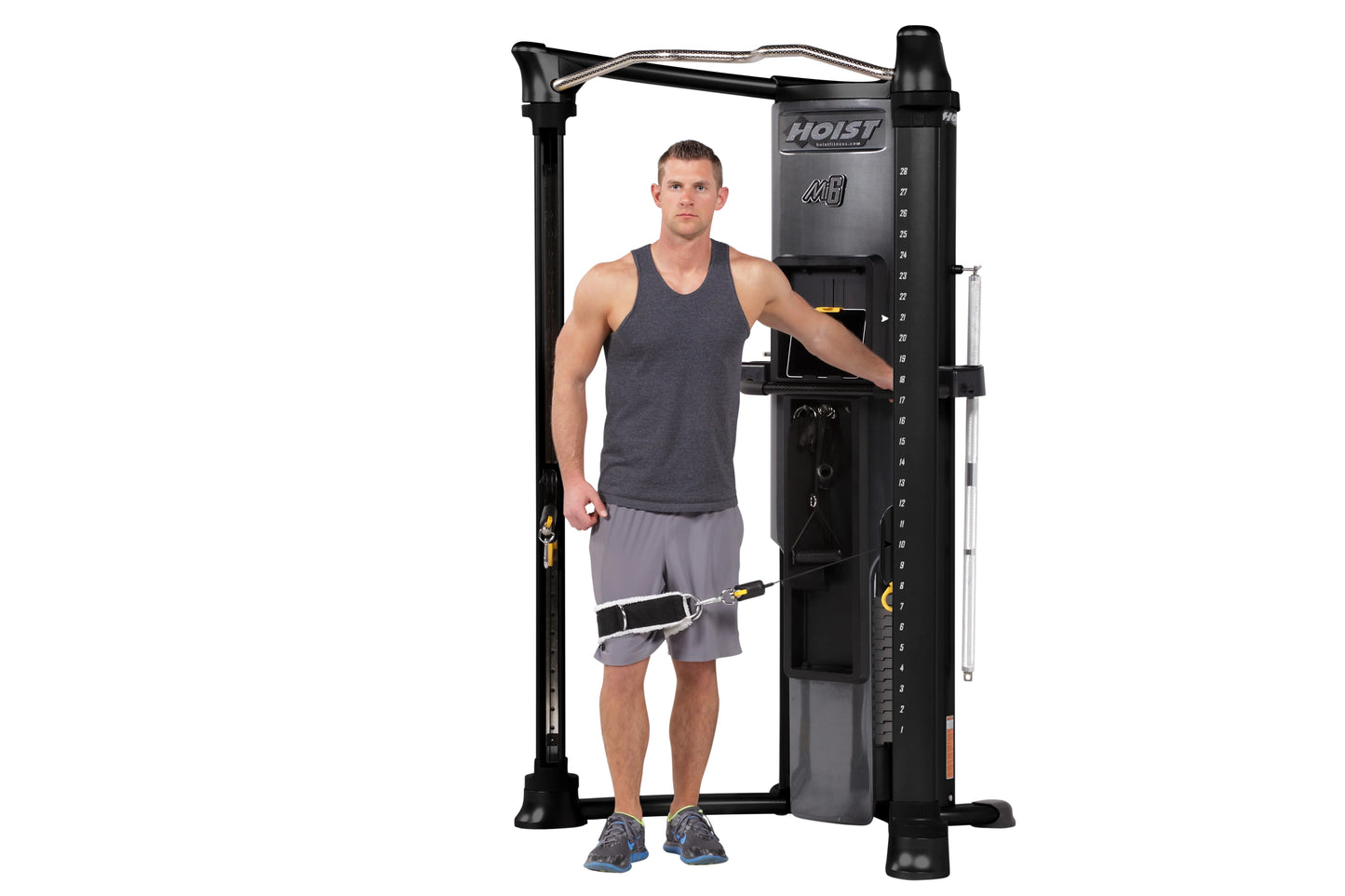 Male model demonstrating Hoist Mi6 functional trainer with dual weight stacks, black frame and cables, on white background