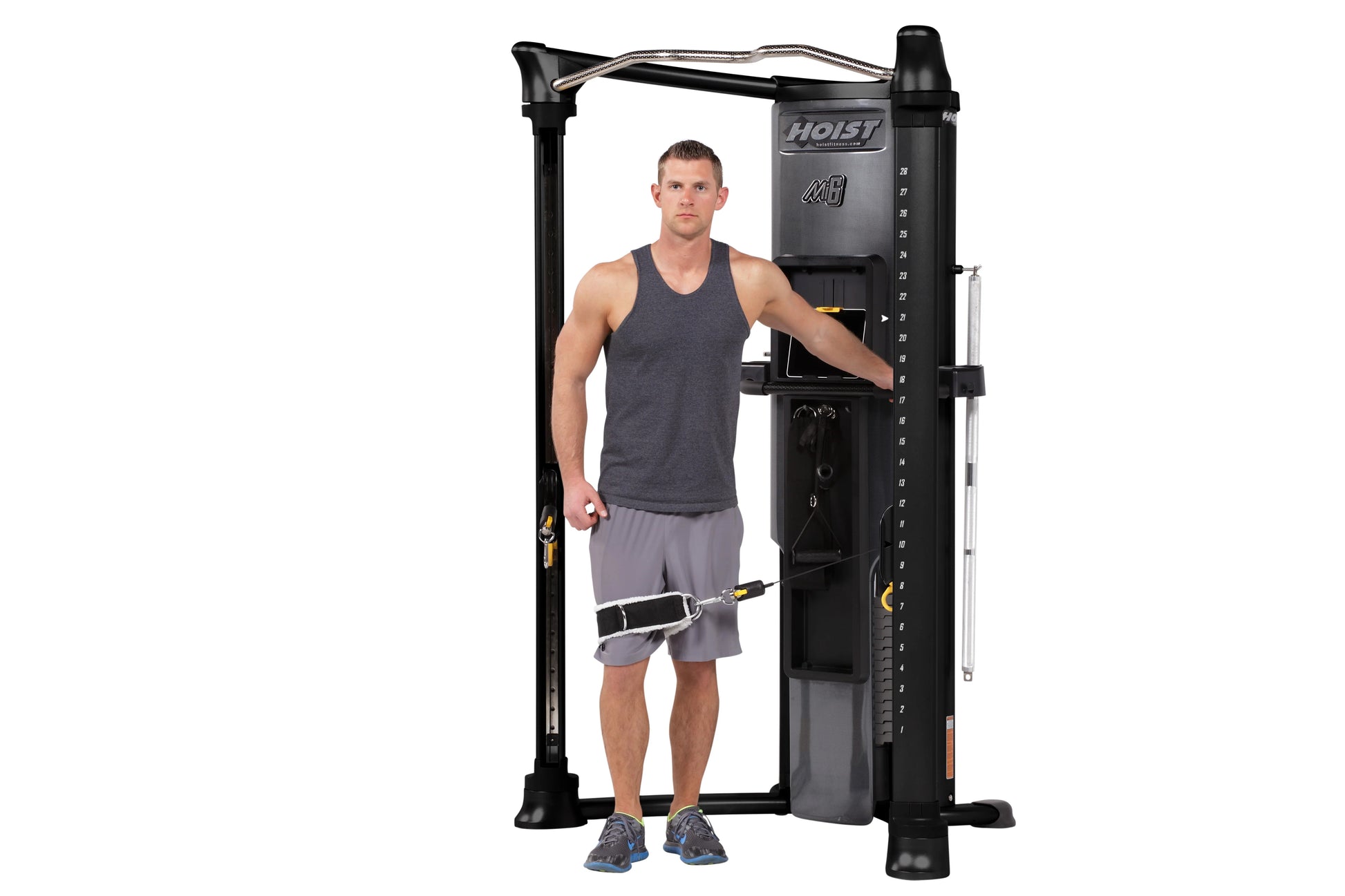 Male model demonstrating Hoist Mi6 functional trainer with dual weight stacks, black frame and cables, on white background