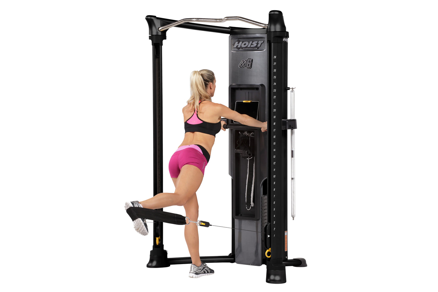 Woman using black Hoist Mi6 functional trainer machine with pink and black athletic wear, demonstrating leg press exercise on